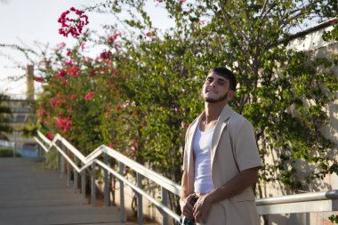 Latin ve İspanyol çocuk, genç ve uyumsuz, asi, bej ceketli ve pantolonlu, elleri kemerinde, kameraya meydan okuyarak poz veriyor. Kavramsal sorunlar, isyan, çeteler.