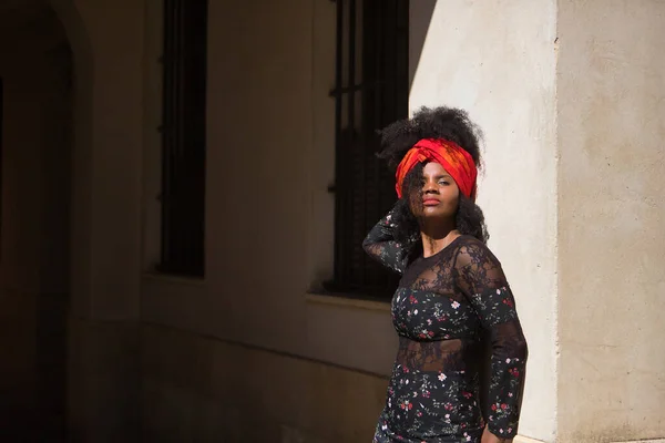 黑黑的女人 一头黑发 头发上戴着花衣和围巾 靠着一面接受太阳光照射的墙 概念美 肖像画 — 图库照片