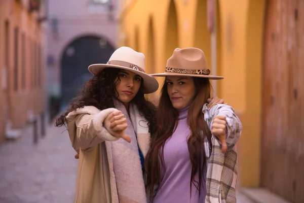 Dwie Kobiety Młode Piękne Kapeluszach Płaszczach Objął Kciuki Dół Znak — Zdjęcie stockowe