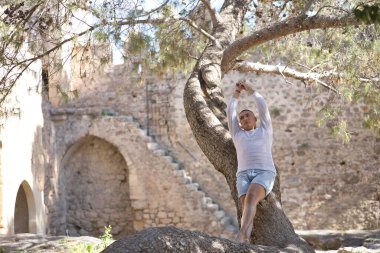İkili olmayan, genç ve Güney Amerikalı, ağır makyajlı, bir ağaç gövdesine yaslanmış, kollarını kaldırmış, rahatlamış, sonsuzluğa bakıyor. Kavram kraliçesi, lgbtq +, gurur, nonoş.