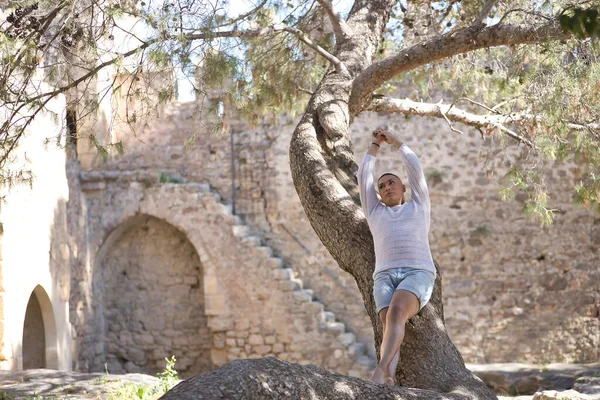İkili olmayan, genç ve Güney Amerikalı, ağır makyajlı, bir ağaç gövdesine yaslanmış, kollarını kaldırmış, rahatlamış, sonsuzluğa bakıyor. Kavram kraliçesi, lgbtq +, gurur, nonoş.