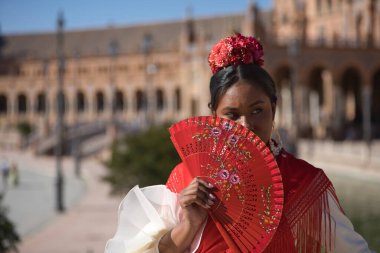 Bej Flamenko çingene kostümü ve kırmızı şallı genç siyah ve Güney Amerikalı bir kadının portresi. İspanya 'da Seville' de bir hayranla güneşten korunuyor. Konsept dansı, folklor, flamenko, sanat