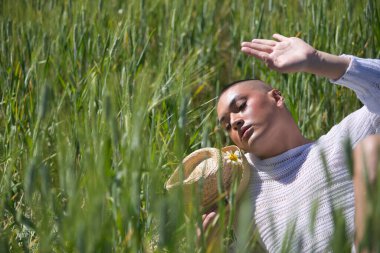 İkili olmayan, genç ve Güney Amerikalı, çok makyajlı, yeşil buğday tarlasının ortasında duruyor. Kavram kraliçesi, lgbtq +, gurur, nonoş.