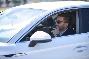 Başarılı, çekici, ceketli ve güneş gözlüklü beyaz lüks arabasında düşünceli davranan genç bir İspanyol. Kavram, arabalar, lüks, başarı, iş adamı.