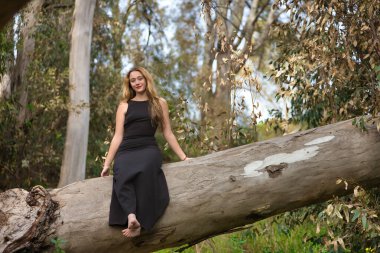 Genç bir kadın, sarışın ve güzel, siyah elbiseli, büyük bir ağacın gövdesinde oturuyor, doğanın ortasında, saf ve bakir. Doğa, huzur, saflık, bekaret, ağaçlar.