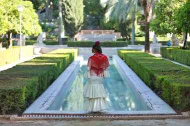 Bej renkli çingene flamenko takım elbiseli ve kırmızı şallı genç siyah ve Güney Amerikalı kadın, İspanya 'nın Seville şehrinde bir parkta poz veriyor. Konsept dansı, folklor, flamenko, sanat.