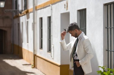 Sakallı, takım elbiseli ve kravatlı çekici genç bir işadamı, beyaz güneşli bir duvara yaslanmış dalgın bir tavırla. Güzelliği, modayı, başarıyı, başarıyı, eğilimi kavra.