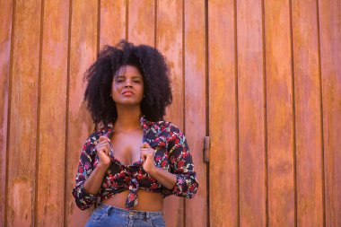 Genç bir kadın, güzel ve siyah saçlı, çiçekli gömlekli tahta bir tahta kapıya yaslanmış, şehvetli, kışkırtıcı ve çapkın bir tavırla. Güzelliği kavrayın, şehveti, kışkırtın, flört edin..