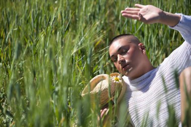 İkili olmayan, genç ve Güney Amerikalı, çok makyajlı, yeşil buğday tarlasının ortasında duruyor. Kavram kraliçesi, lgbtq +, gurur, nonoş.
