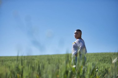 Genç, Güney Amerikalı, ikili olmayan, ağır makyajlı, yeşil buğday tarlasının ortasında doğal papatyalarla beyaz bir kazak içinde poz veren. Kavram kraliçesi, lgbtq +, gurur, nonoş.