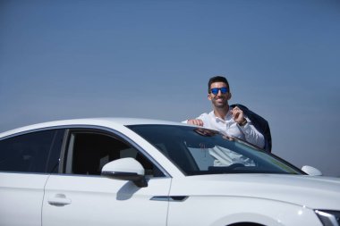 Başarılı, çekici, beyaz gömlekli ve ceketli, beyaz gözlüklü beyaz lüks arabasının çatısına dayanan İspanyol bir adam. Kavram, arabalar, lüks, başarı, iş adamı.