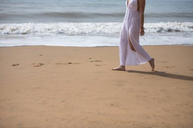 Genç bir kadının bacakları, beyaz elbiseli, yalnız bir sahilde yürüyen, sakin ve sakin. Huzuru, huzuru, yalnızlığı, kendini bulmayı kabul et..