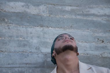 Latin and Hispanic boy, young and nonconformist, rebellious, with a handkerchief on his head, exhaling the smoke of a cigarette rolled by himself. Concept tobacco, smoke, fire, addiction, gangs.