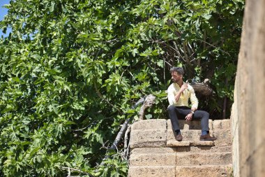 Sakallı, sarı gömlekli, siyah pantolonlu ve güneş gözlüklü genç ve çekici iş adamı, düşünceli bir tavırla taş merdivenlerde oturuyor. Güzelliği, modayı, başarıyı, başarıyı, eğilimi kavra.