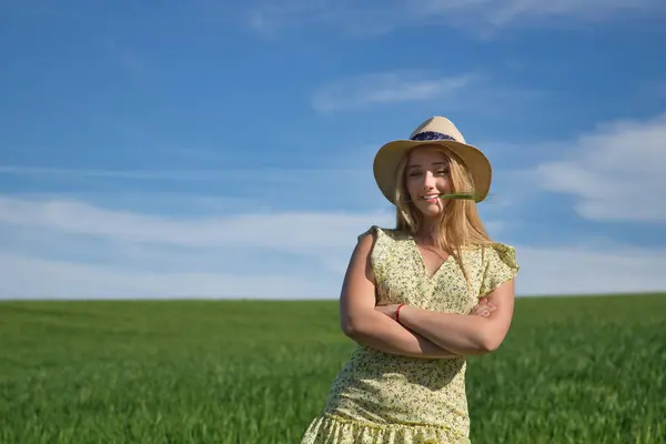 Farm woman, young, beautiful and blonde in a yellow dress, with an ear in her mouth in the middle of a green wheat field, very smiling and happy. Concept beauty, happiness, peace, fields, meadows.