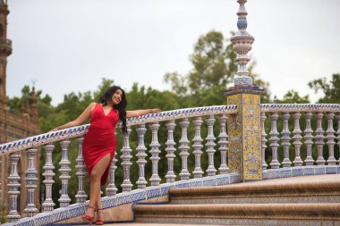 Güney Amerikalı bir kadın, genç, güzel, esmer, zarif kırmızı elbiseli, İspanya meydanında model olarak poz veriyor. Güzellik, moda, trend, etnik köken, çeşitlilik, zarafet kavramı.
