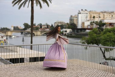 Genç bir kadın, İspanyol, güzel, esmer, zarif bir menekşe elbisesi olan, elbisesini uçurmak için komik kıvrımlar yapan. Güzellik kavramı, moda, trend, zarafet, antika.