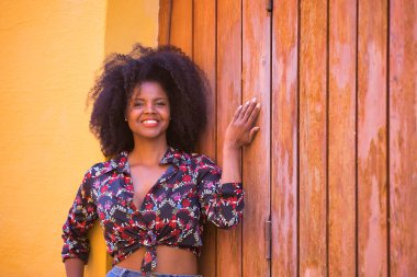 Genç bir kadın, güzel ve siyah, afro saçlı, çiçekli gömlekli tahta tahta kapıya dayanmış, sessiz, mutlu ve gülümseyen. Güzelliği, huzuru, mutluluğu kavra..