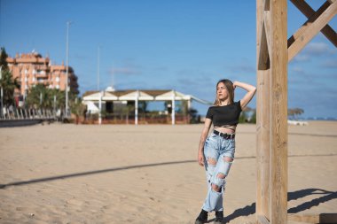 Genç, güzel, sarışın, yeşil gözlü, siyah bluzlu, yırtık kot pantolon ve dövmeli, tahta bir direğe yaslanmış, yalnız, sakin ve rahat. Yalnızlık, huzur, sükunet kavramı.