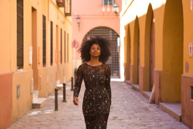 Genç, güzel, siyah saçlı, çiçekli elbiseli, yalnız bir caddede yürüyen, güçlü ve bağımsız bir kadın. Kavram güçlendirme, güvenlik, başarı, bağımsızlık, güzellik.