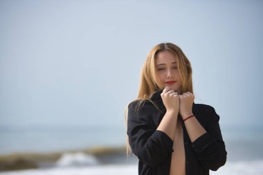 Genç bir kadın, sarışın ve güzel, bikini ve siyah gömlek giyiyor, gömleğinin yakasını tutuyor, kendini seviyor. Saflık, bekaret, koruma kavramı.