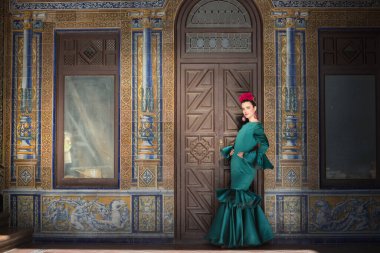 Genç, güzel, sarışın, tipik yeşil renkli flamenko takım elbiseli, arkasında güzel fayanslarla poz veren bir kadın. Flamenko konsepti, tipik İspanyolca, Sevilla, Endülüs.