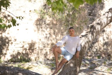 İkili olmayan, genç, Güney Amerikalı, aşırı makyajlı, bir ağaç gövdesine yaslanmış, rahatlamış, kameraya bakıyor. Kavram kraliçesi, lgbtq +, gurur, nonoş.