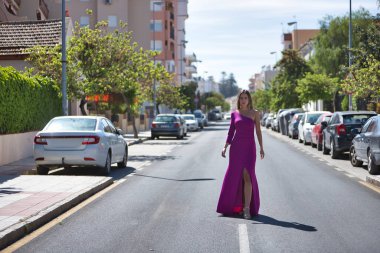 Mor elbiseli, topuklu ayakkabılı, şehir yolunda poz veren genç ve güzel bir kadın. Güzelliği, modayı, eğilimi kavra.