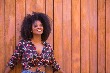Genç bir kadın, güzel ve siyah, afro saçlı, çiçekli gömlekli tahta tahta kapıya dayanmış, sessiz, mutlu ve gülümseyen. Güzelliği, huzuru, mutluluğu kavra..