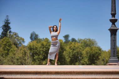 Güney Amerikalı bir kadın, genç, güzel, gri bluzlu ve etekli esmer, caddenin ortasında model gibi poz veren, mutlu ve kaygısız. Güzelliği, modayı, eğilimi, çeşitliliği kavra.