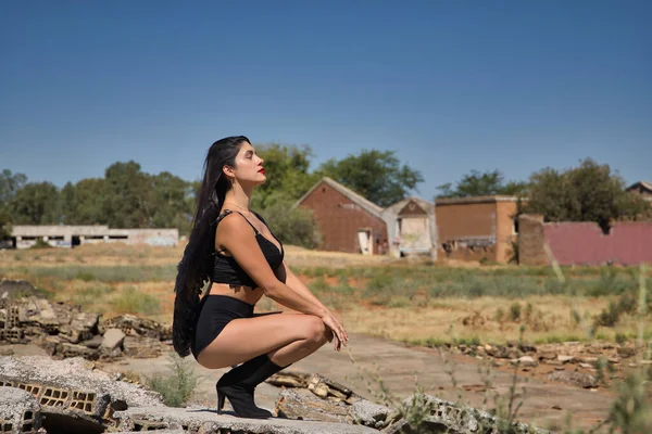 South American woman, young, beautiful, brunette with lingerie and black wings, posing crouching receiving sun rays in the middle of the ruins of a building. Concept angels, beauty, costumes, wings.
