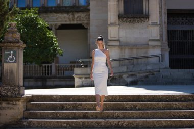 Beyaz takım elbiseli, topuklu ayakkabılı genç, güzel, sarışın bir kadın, merdivenlerden iniyor, kendinden emin ve kendinden emin. Güzellik, moda, moda, model konsepti.