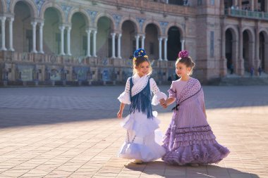 Sevilla 'da güzel bir meydanda tipik bir flamenko elbiseyle yürüyen ve mutlu bir şekilde konuşan iki kız. Dans konsepti, flamenko, tipik İspanyolca, Sevilla, İspanya.
