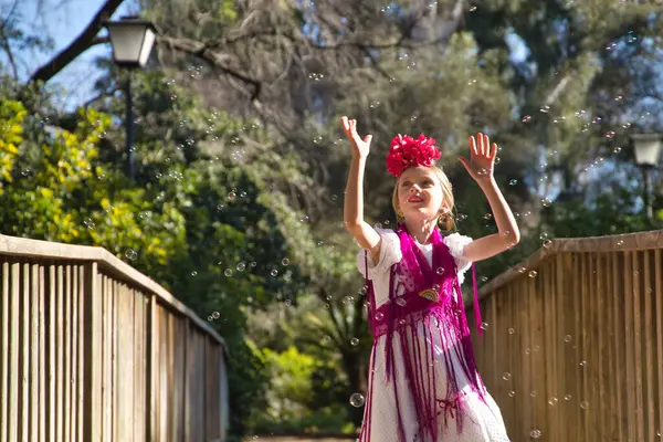 Flamenko yapan, sabun köpüğüyle oynayan, tipik flamenko elbisesiyle tahta bir köprüde dans eden bir kız. Konsept dansı, flamenko, tipik İspanyolca, Sevilla, İspanya.