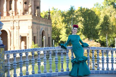 Genç, güzel, sarışın, tipik yeşil renkli flamenko takım elbiseli, bir köprünün üzerindeki fayanslı korkuluklara yaslanmış poz veriyor. Flamenko konsepti, tipik İspanyolca, Sevilla, Endülüs.