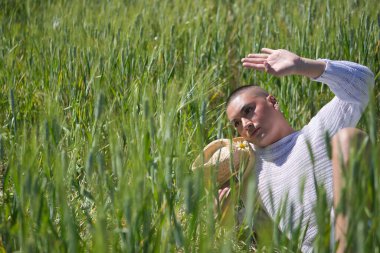 İkili olmayan, genç ve Güney Amerikalı, çok makyajlı, yeşil buğday tarlasının ortasında duruyor. Kavram kraliçesi, lgbtq +, gurur, nonoş.