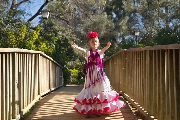 Flamenko yapan, sabun köpüğüyle oynayan, tipik flamenko elbisesiyle tahta bir köprüde dans eden bir kız. Konsept dansı, flamenko, tipik İspanyolca, Sevilla, İspanya.