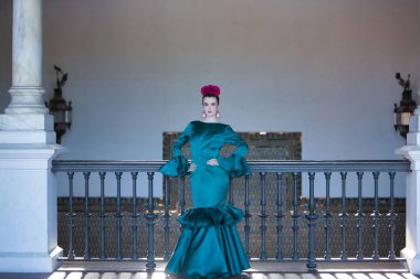 Genç, güzel, sarışın, tipik yeşil renkli flamenko takım elbiseli, demir parmaklıkların yanında poz veriyor. Flamenko konsepti, tipik İspanyolca, Sevilla, Endülüs.