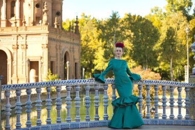 Genç, güzel, sarışın, tipik yeşil renkli flamenko takım elbiseli, bir köprünün üzerindeki fayanslı korkuluklara yaslanmış poz veriyor. Flamenko konsepti, tipik İspanyolca, Sevilla, Endülüs.