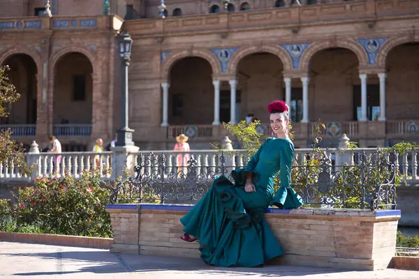 stock image Young, pretty, blonde woman in typical green colored flamenco suit, posing sitting on a tiled and brick bench. Flamenco concept, typical Spanish, Seville, Andalusia.
