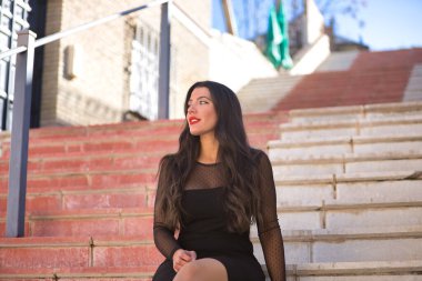 Endülüs 'ün güzel beyaz bir köyünün merdivenlerinde oturan zarif, siyah elbiseli, dikkati dağınık bakışlı genç, güzel, esmer kadın. Güzellik, moda, trend, seyahat, kırsal.