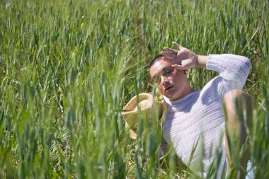 İkili olmayan, genç ve Güney Amerikalı, çok makyajlı, yeşil buğday tarlasının ortasında duruyor. Kavram kraliçesi, lgbtq +, gurur, nonoş.