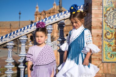 İki kız flamenko yapıyor, biri kameraya bakıyor diğeri de Seville 'de güzel bir meydanda merdivenlerde tipik flamenko kostümlü ortağa bakıyor. Dans konsepti, flamenko..