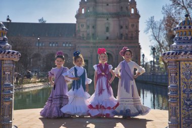 Flamenko yapan dört kız, kameraya bakarak poz veriyorlar, tipik flamenko kostümleriyle Sevilla 'da güzel bir meydanda gölün yanında. Konsept dansı, flamenko, tipik İspanyolca, Sevilla, İspanya.