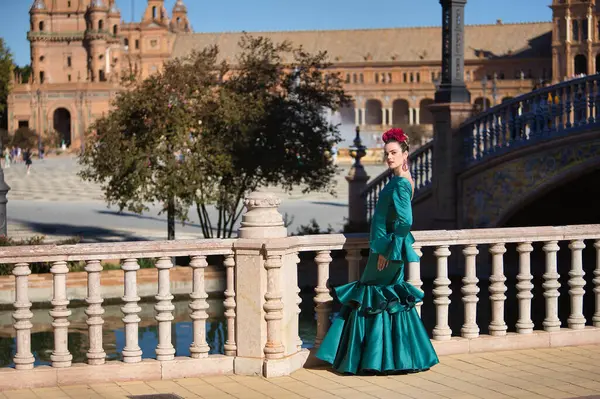 stock image Young, pretty, blonde woman in typical green colored flamenco suit, posing leaning on a stone railing. Flamenco concept, typical Spanish, Seville, Andalusia.