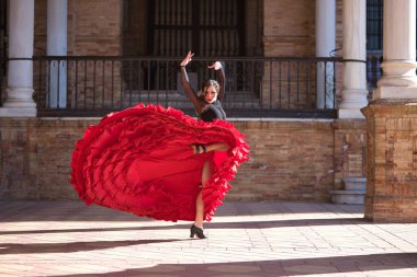 Genç, güzel, esmer, siyah gömlekli, kırmızı etekli, İspanya meydanında mermer sütunlar arasında flamenko dansı yapan bir kadın. Flamenko konsepti, dans, sanat, tipik İspanyolca.