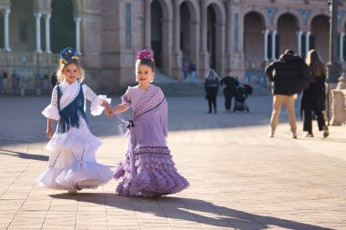 Sevilla 'da güzel bir meydanda tipik bir flamenko elbiseyle yürüyen ve mutlu bir şekilde konuşan iki kız. Dans konsepti, flamenko, tipik İspanyolca, Sevilla, İspanya.