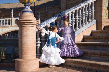 İki kız flamenko dansı yapıyor. Sevilla 'da güzel bir meydanda merdivenlerde tipik flamenko kostümleriyle birbirlerine bakıyorlar. Dans konsepti, flamenko, tipik İspanyolca, Sevilla, İspanya.