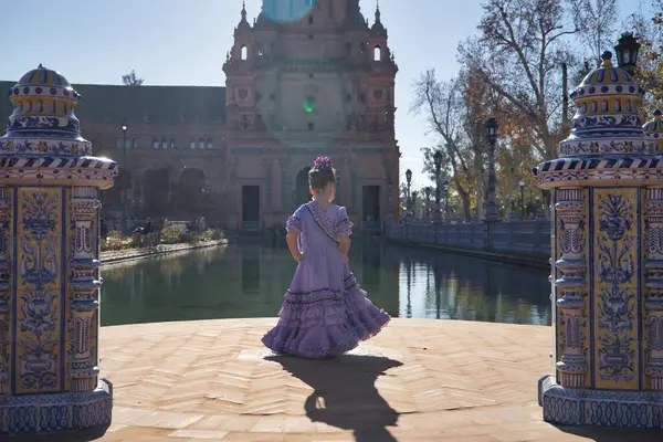 stock image A girl dancing flamenco, in typical flamenco dress, with her back turned, receiving the sun's rays, next to a lake in a beautiful square in Seville. Concept dance, flamenco, typical Spanish, Spain.