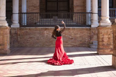 Genç, güzel, esmer, siyah gömlekli, kırmızı etekli, İspanya meydanında mermer sütunlar arasında flamenko dansı yapan bir kadın. Flamenko konsepti, dans, sanat, tipik İspanyolca.